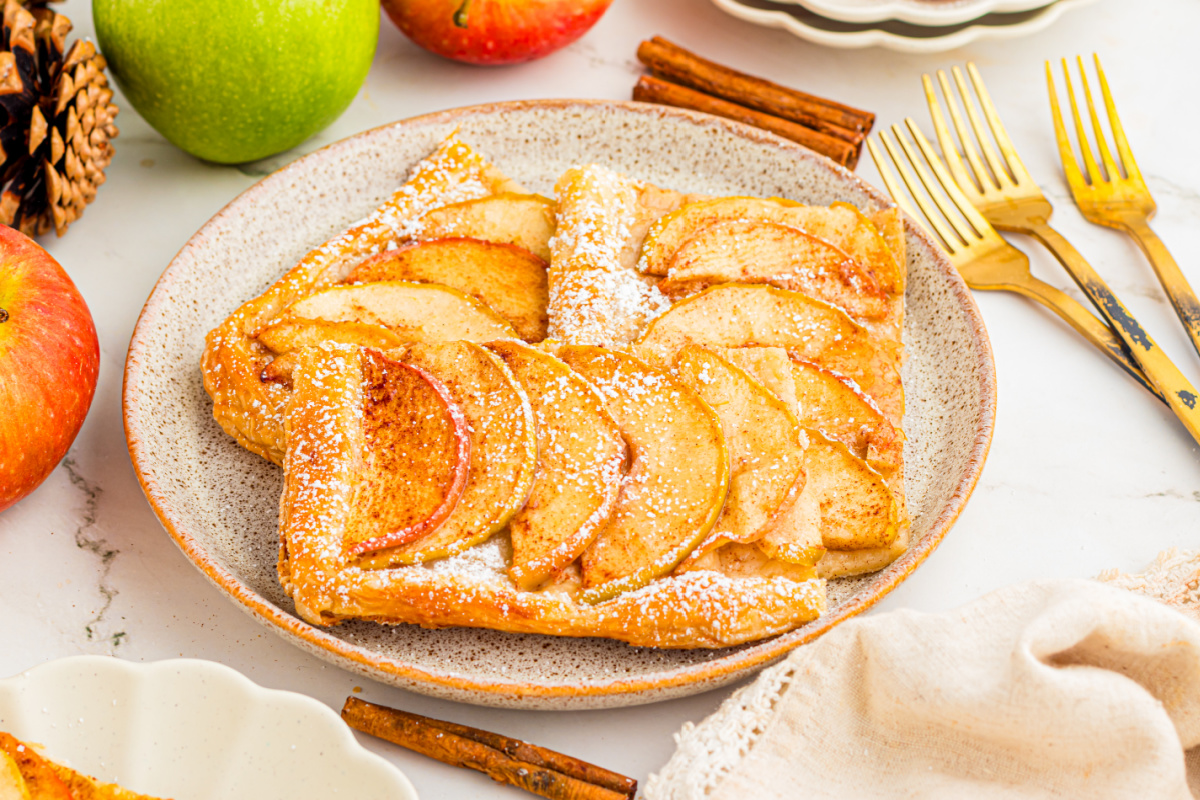 Golden puff pastry tart topped with thinly sliced cinnamon apples Slices of puff pastry apple tart topped with cinnamon apples and powdered sugar