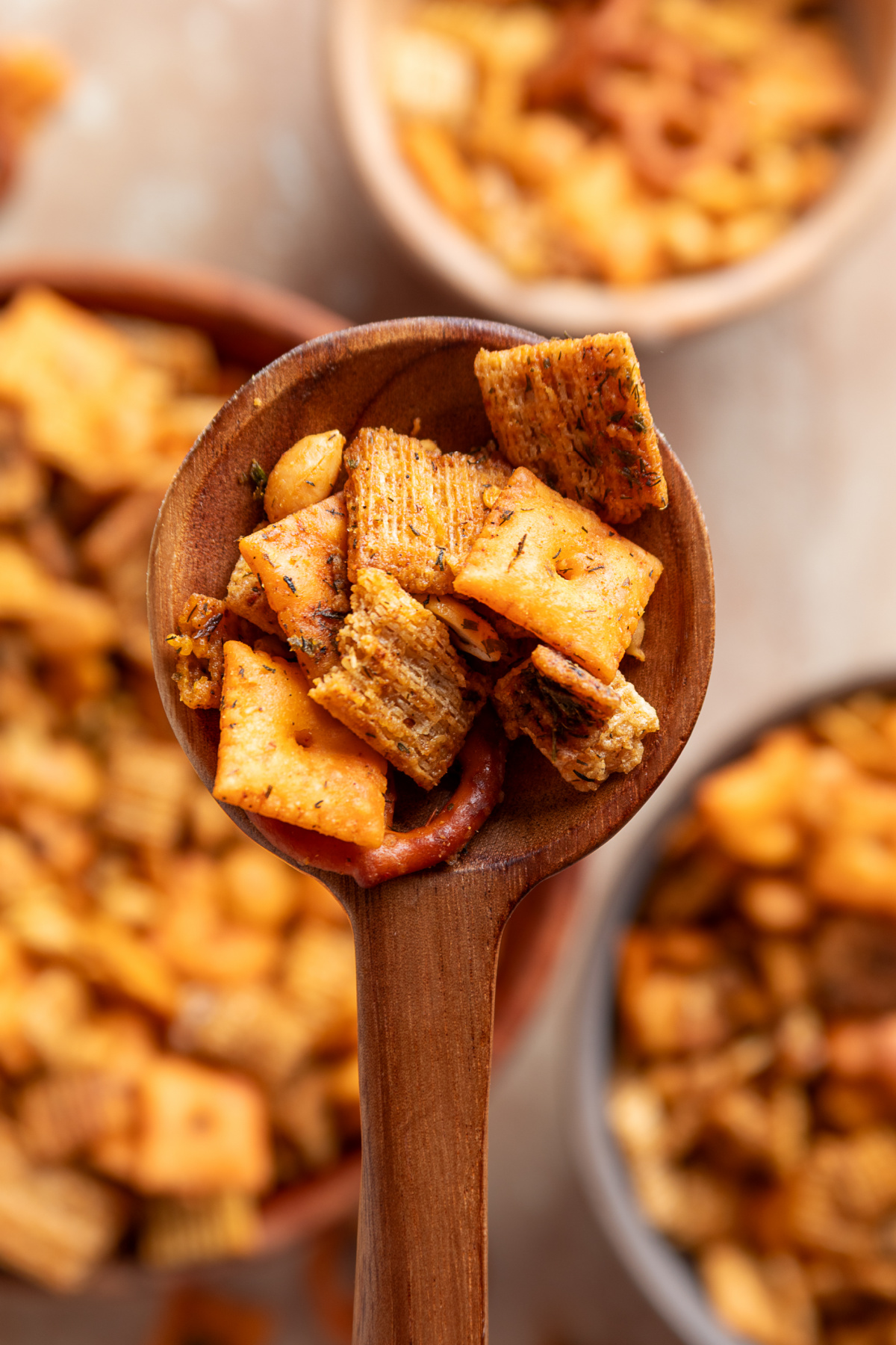 Wooden spoon filled with seasoned Chex cereal, Cheez-It crackers, Triscuit pieces and a pretzel
