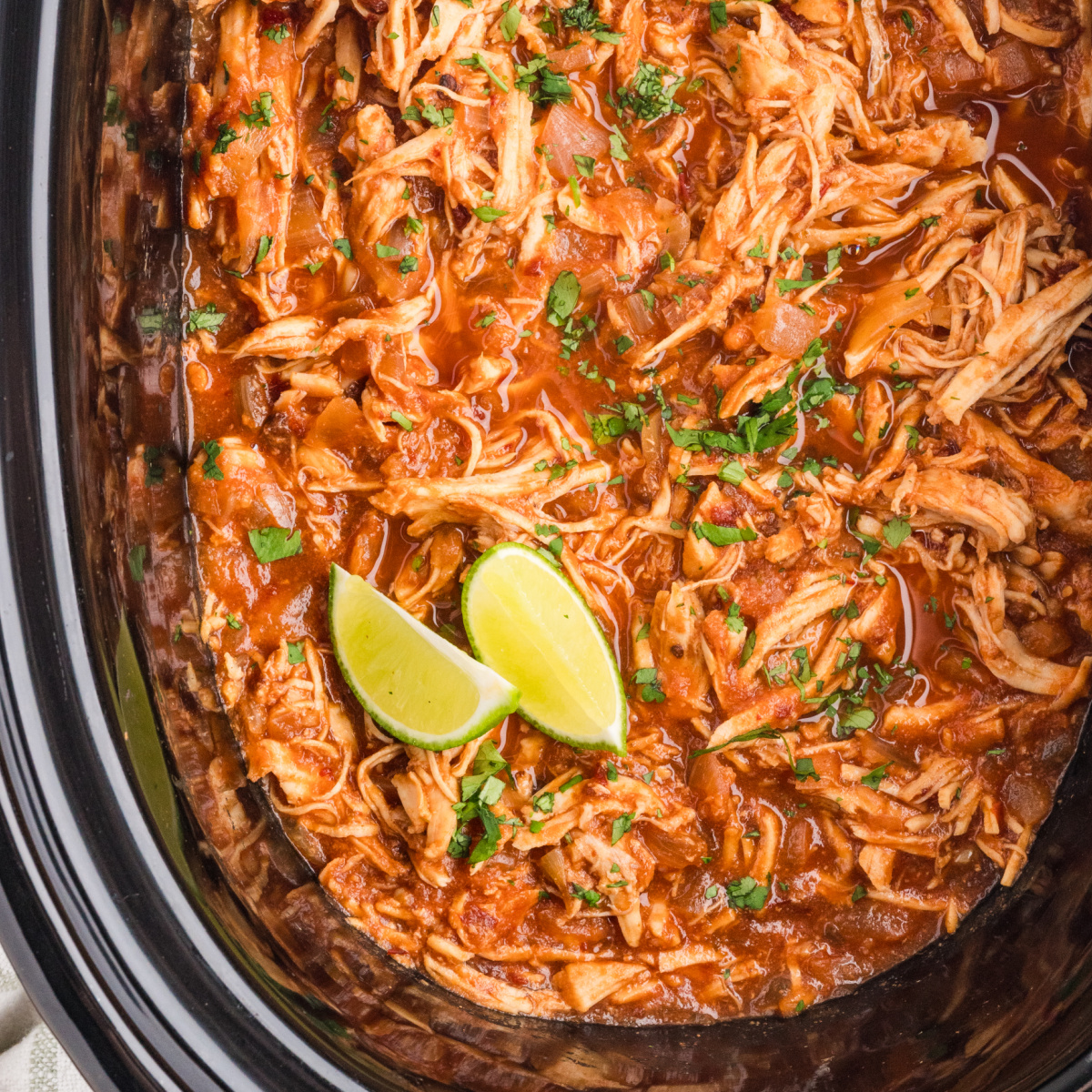 Slow cooker chipotle chicken with shredded chicken, cooked onions, cilantro and fresh lime wedges