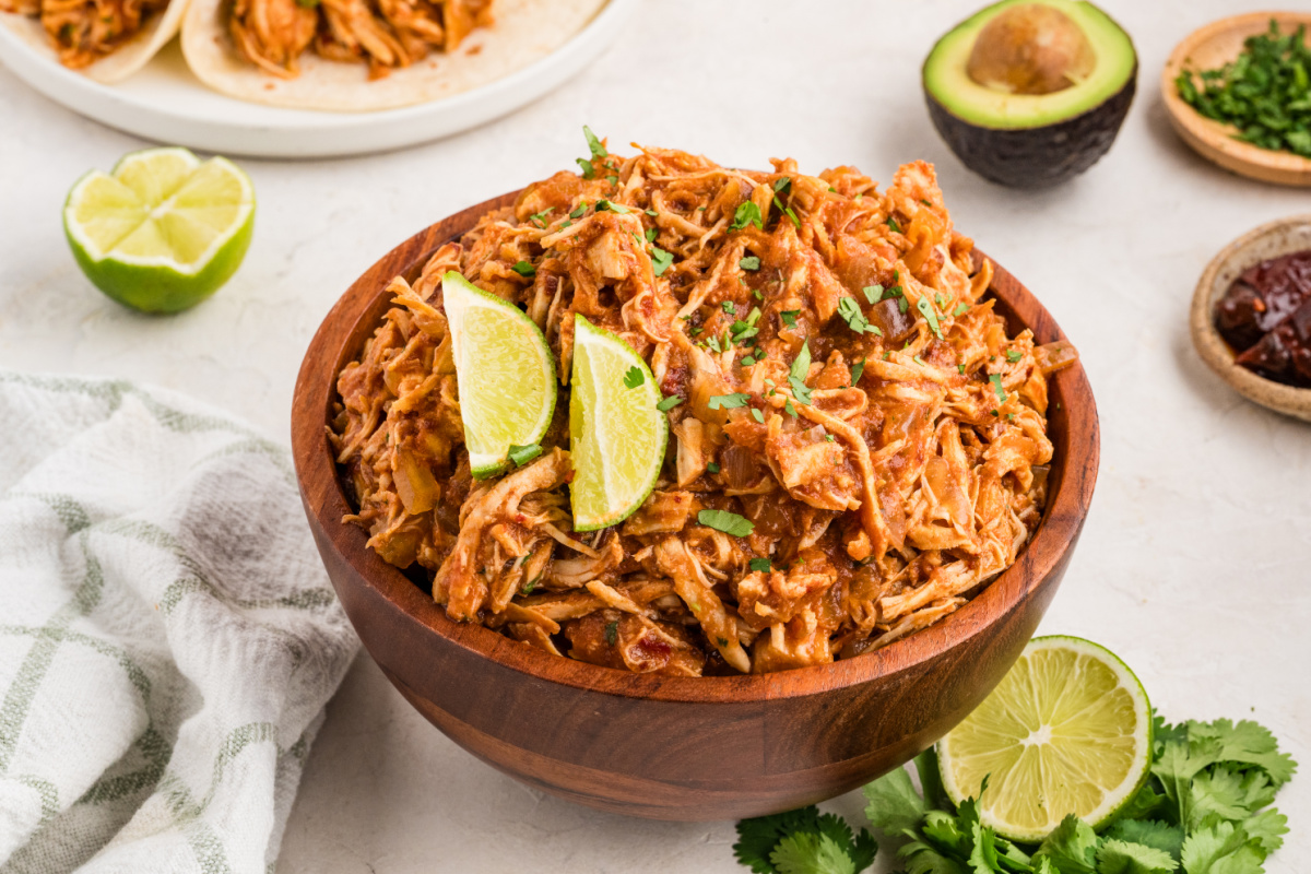 Slow cooker chipotle chicken in a wooden serving bowl with fresh lime and cilantro