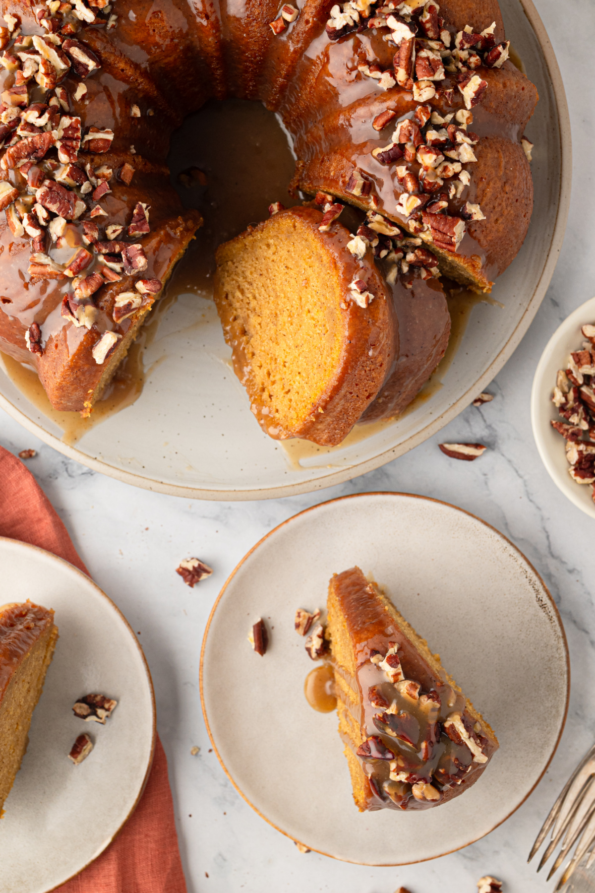 Cut sweet potato Bundt cake showing the soft interior beneath buttered rum caramel and toasted pecans. Sweet potato Bundt cake with a slice removed and served on a plate, topped with buttered rum caramel and toasted pecans.