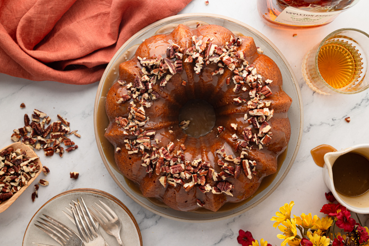 Roasted sweet potato Bundt cake finished with buttered rum caramel and toasted pecans, served alongside dark rum. Overhead view of sweet potato Bundt cake with buttered rum caramel, toasted pecans and dark rum alongside.