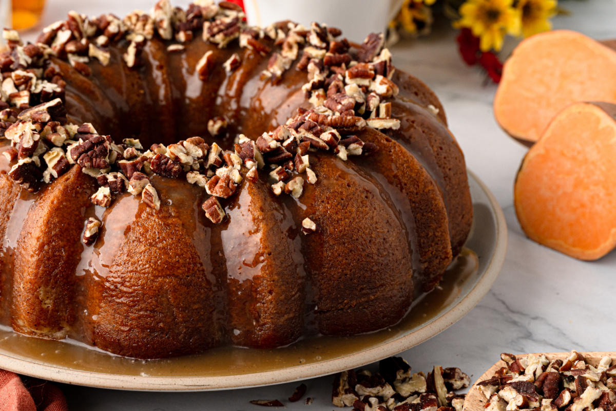 Finished brown butter sweet potato Bundt cake with dark rum caramel, toasted pecans and fresh sweet potatoes. Sweet potato Bundt cake covered with buttered rum caramel and toasted pecans with cut sweet potatoes alongside.