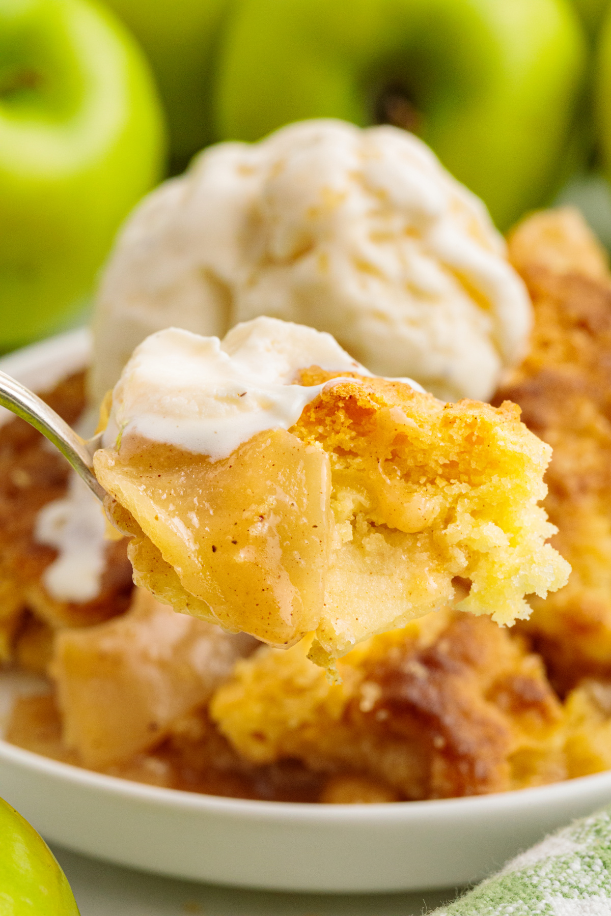 Warm Granny Smith apple filling and butter cake topping with vanilla ice cream melting over the spoonful. Spoonful of warm cinnamon apple filling and soft butter cake topping with melting vanilla ice cream.