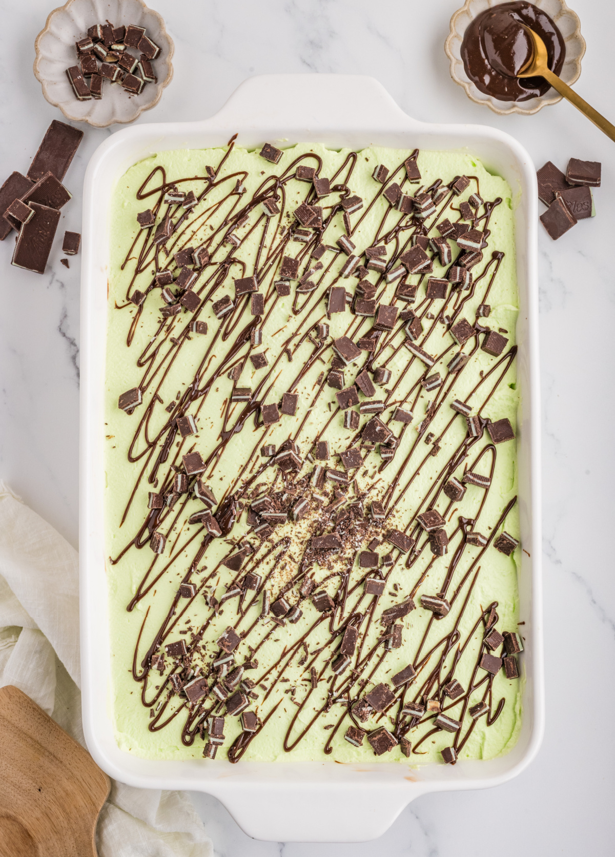 Finished chocolate poke cake in a 9&times;13-inch baking dish topped with pale green mint whipped cream, chopped Andes mints and hot fudge drizzle.