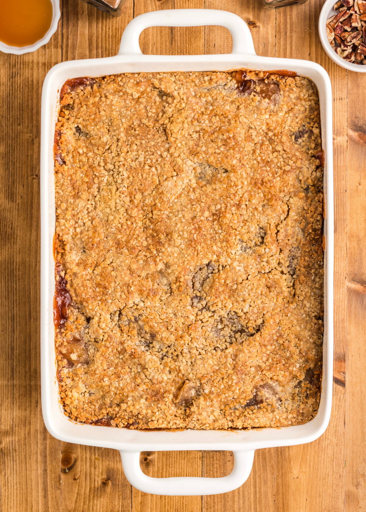 The finished apple dessert has a golden oatmeal cookie crust with cracks across the surface and cinnamon apple filling visible underneath. Baked apple crisp dump cake in a white baking dish with a golden, cracked oatmeal cookie topping.