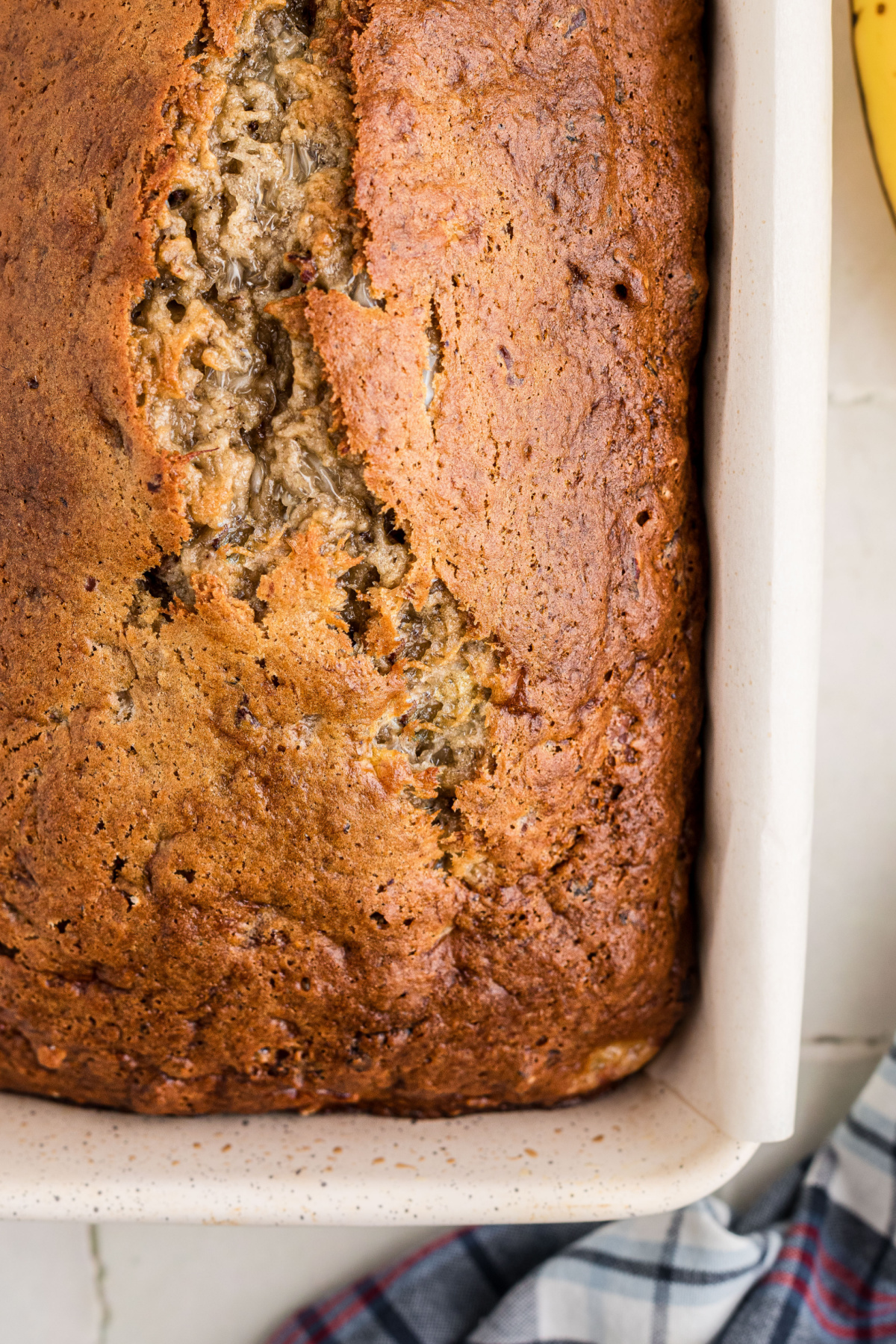 Overhead view of a homemade banana bread loaf with a deep golden brown top and a crack down the center.