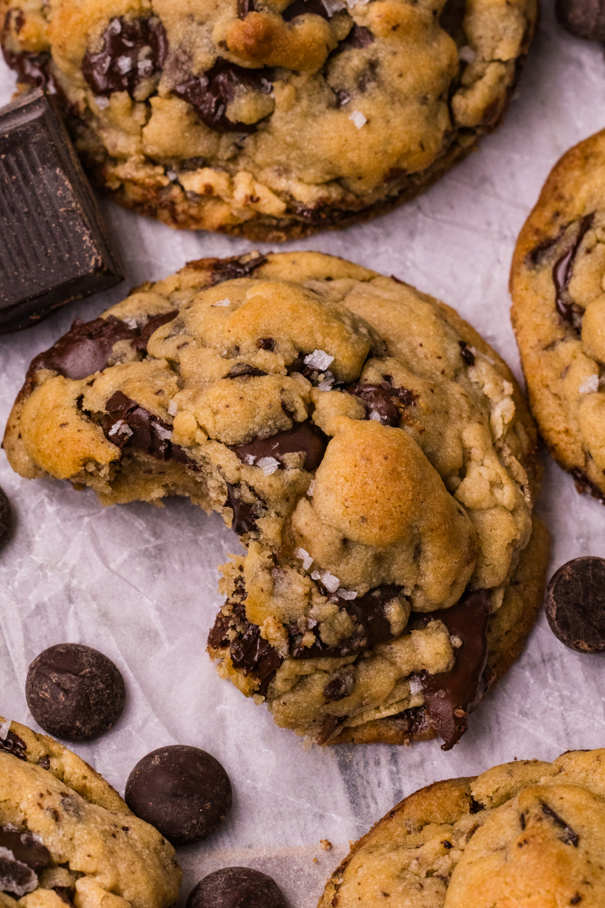 Close-up of a chocolate chip cookie with a bite taken out, showing its soft center, melted chocolate, golden top, and flaky sea salt.