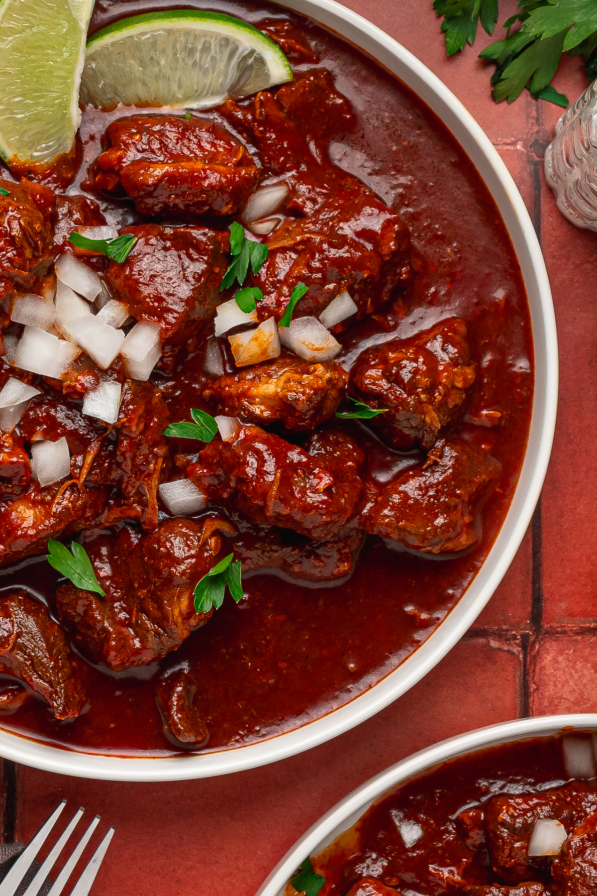 Carne adovada with pork shoulder in red chile sauce topped with onion and parsley