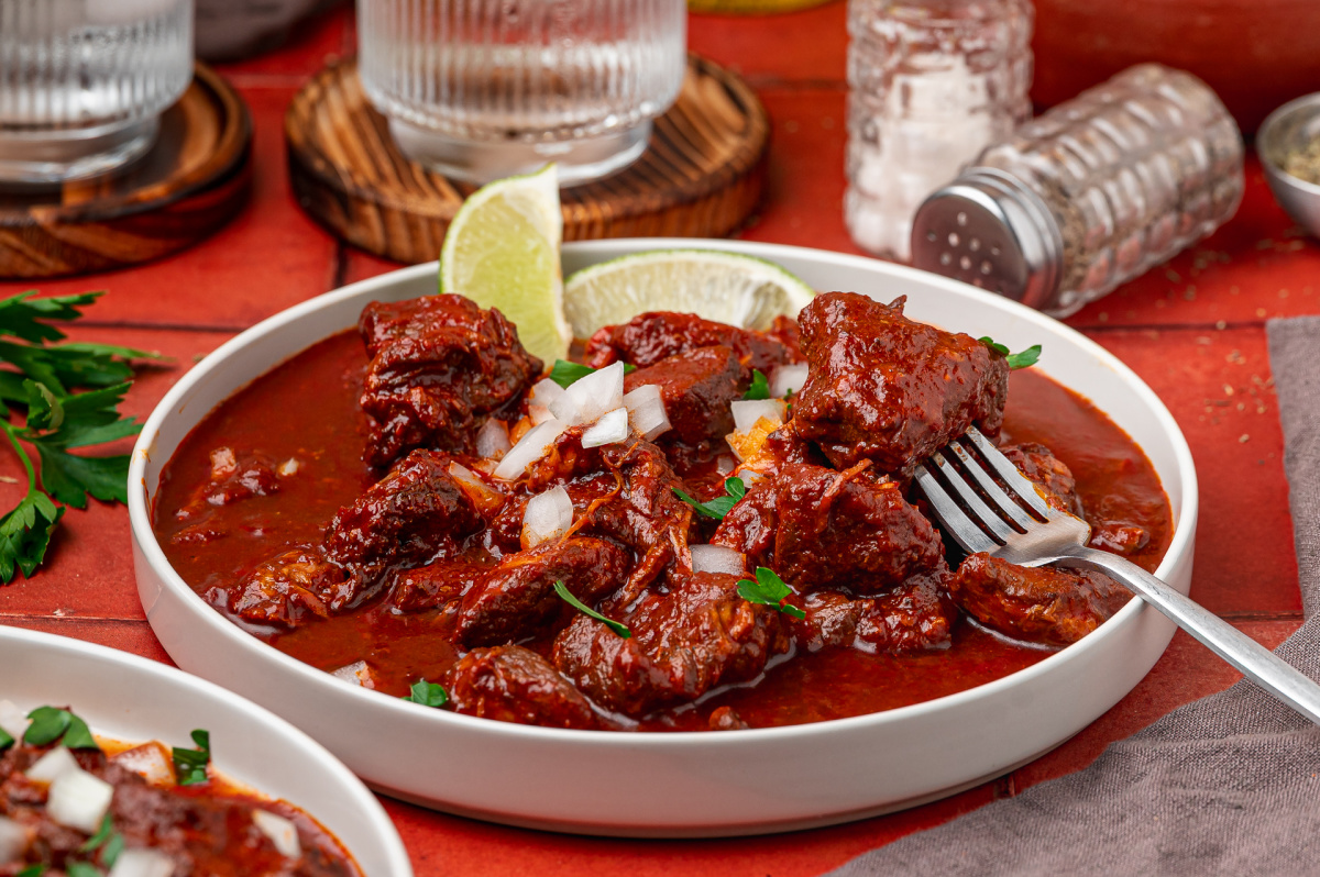 Fork holding tender pork from carne adovada in a red chile sauce