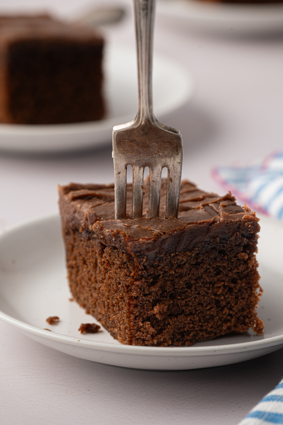 Chocolate Sheet Cake with Thick Brown Butter Frosting Thick square of chocolate sheet cake on a white plate with a fork pressed into the brown butter fudge frosting.