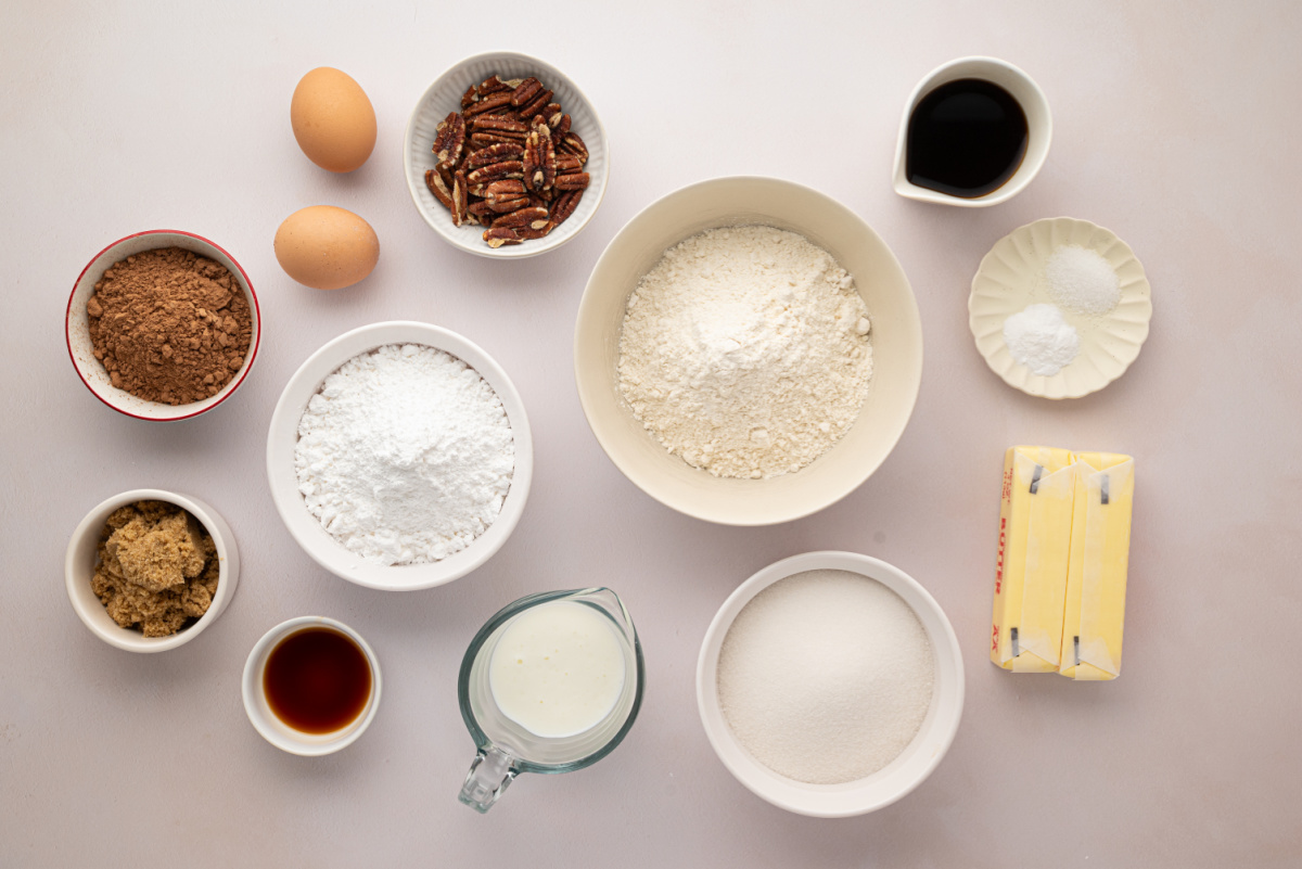 Ingredients for Chocolate Buttermilk Texas Sheet Cake Ingredients for a chocolate Texas sheet cake arranged in bowls, including cocoa powder, buttermilk, butter, flour, sugars, eggs, coffee, and pecans.