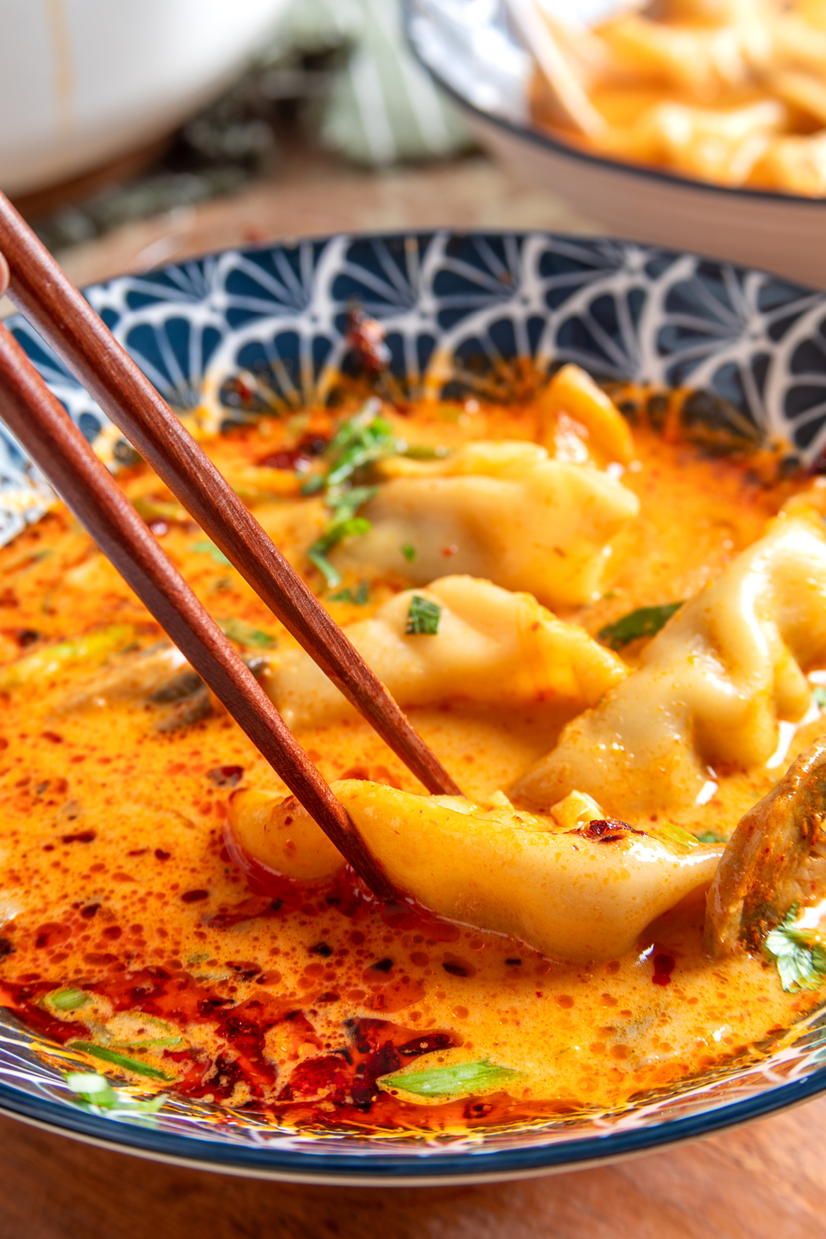 Thai Dumpling Soup with Pork Potstickers and Chili Crisp Close-up of Thai Dumpling Soup with a pork potsticker held by chopsticks over creamy coconut curry broth with chili crisp.