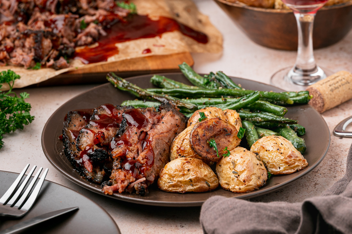 Coffee Rubbed Oven Brisket served with roasted baby potatoes, green beans, and barbecue sauce on a dinner plate.