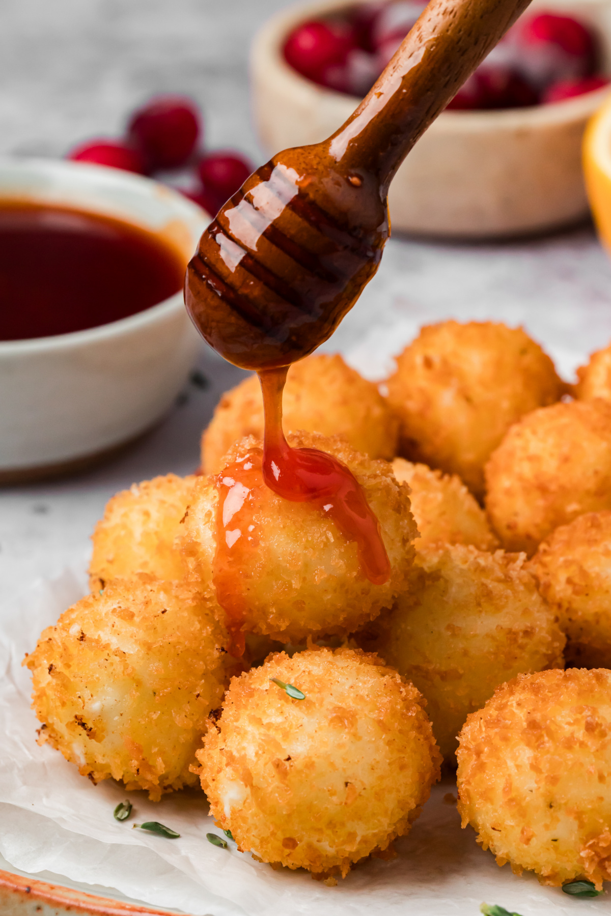 Cranberry Hot Honey Drizzled Over Crispy Goat Cheese Cranberry hot honey dripping from a wooden honey dipper onto a golden panko-crusted goat cheese ball.