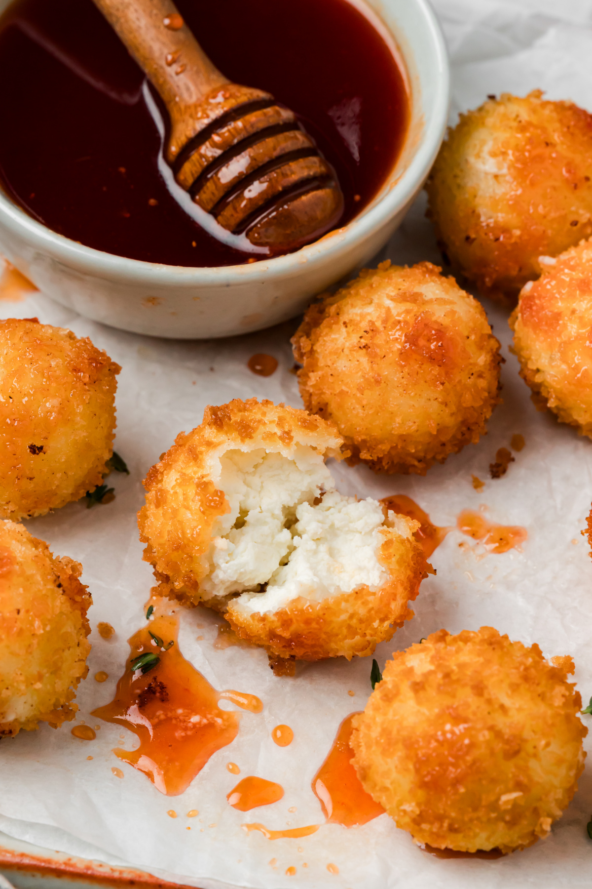 Creamy Goat Cheese Center with Cranberry Hot Honey Fried panko-coated goat cheese ball broken open to show its creamy white center, surrounded by cranberry hot honey and more golden cheese balls.