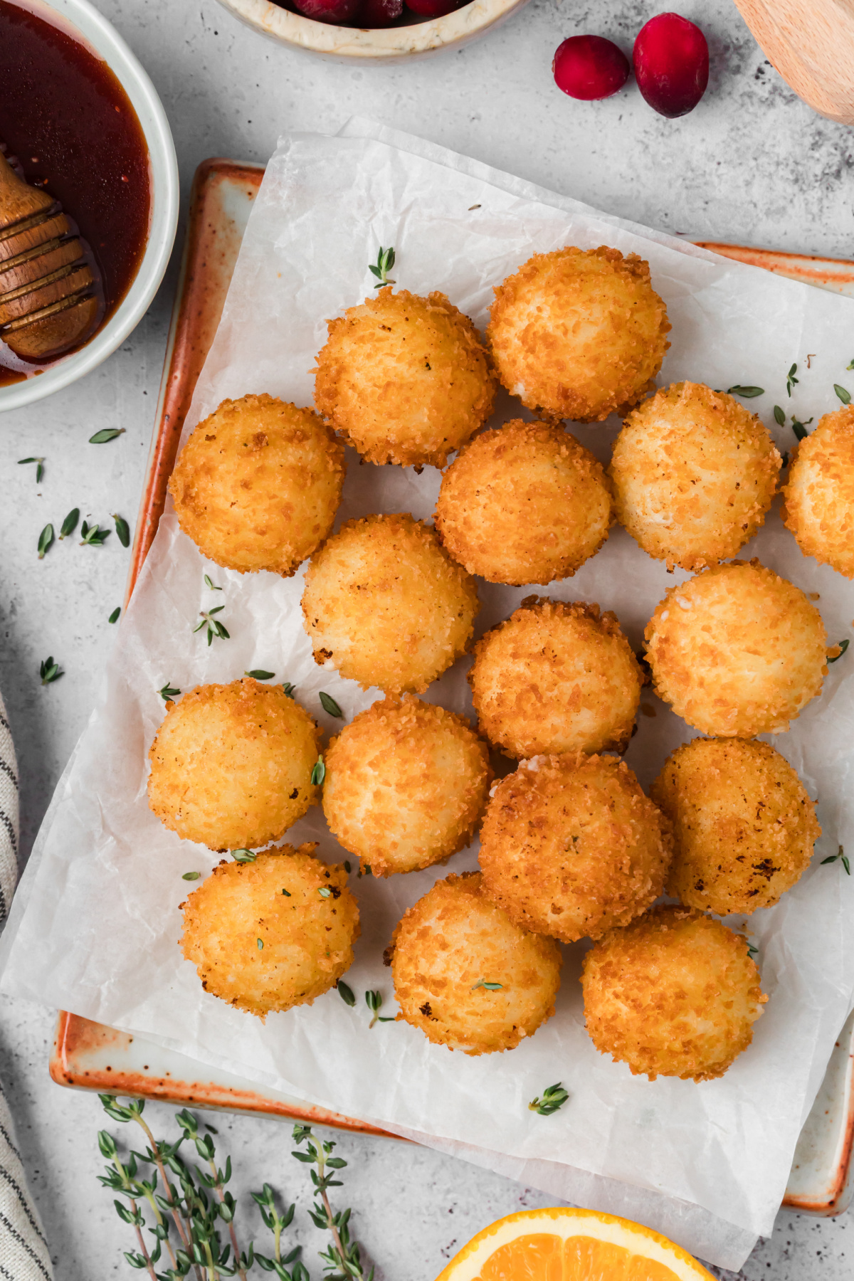 Golden Panko-Crusted Goat Cheese Balls Ready for Serving Overhead view of golden panko-crusted goat cheese balls on a parchment-lined platter with cranberry hot honey and fresh thyme.