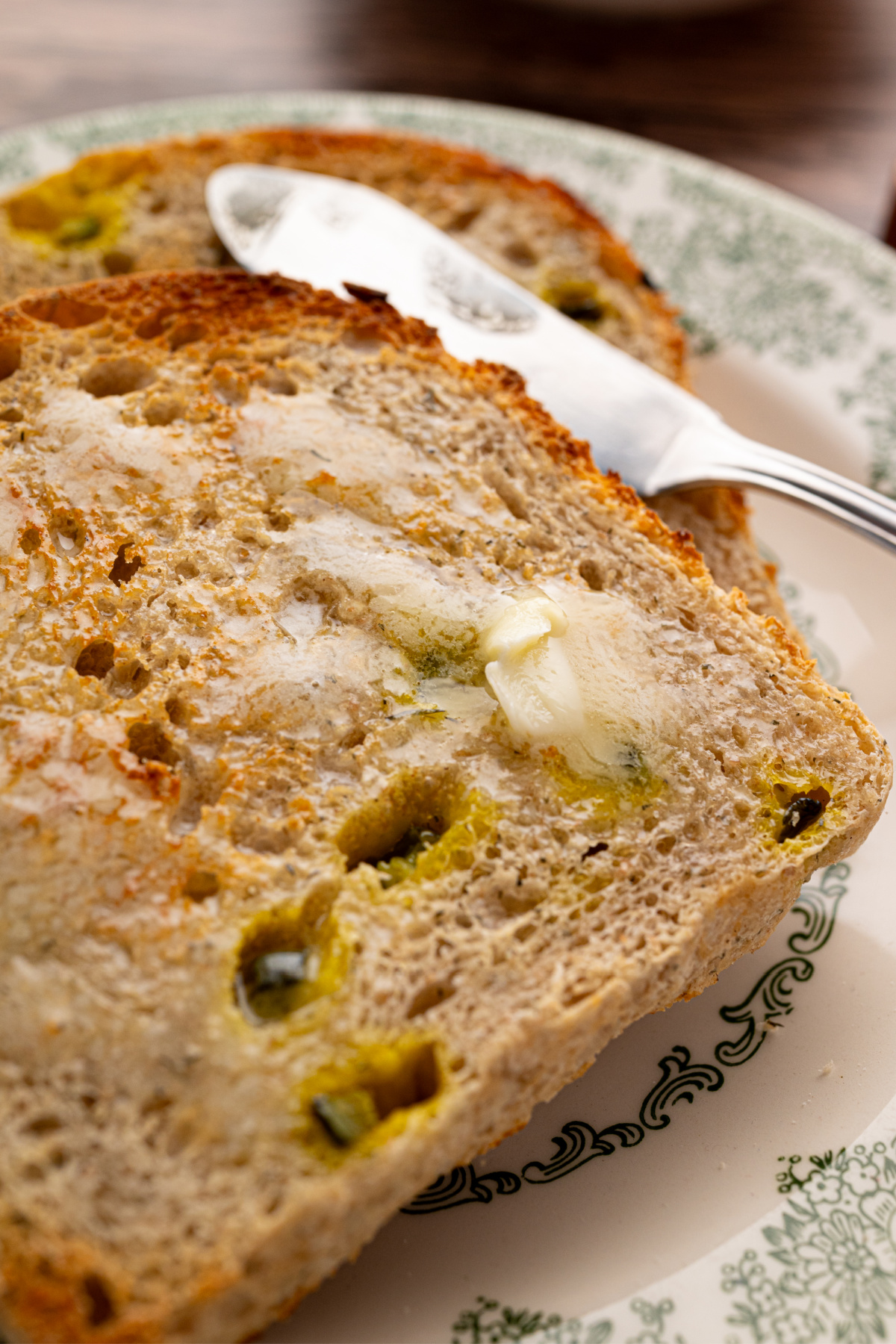 Toasted dill pickle sourdough sandwich bread with melted butter and visible pieces of dill pickle on a plate.