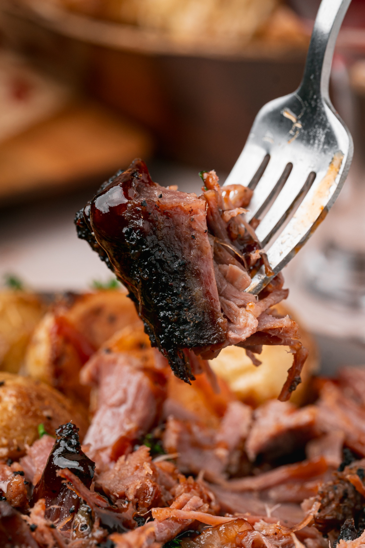 Close-up of tender pulled brisket with dark coffee crust and barbecue sauce on a fork above a dinner plate.