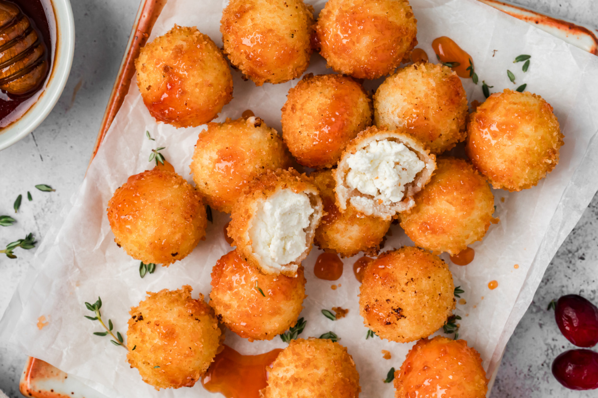 Fried Goat Cheese Balls with Creamy Centers and Cranberry Hot Honey Overhead view of fried goat cheese balls drizzled with cranberry hot honey, with two cut open to reveal their creamy centers.