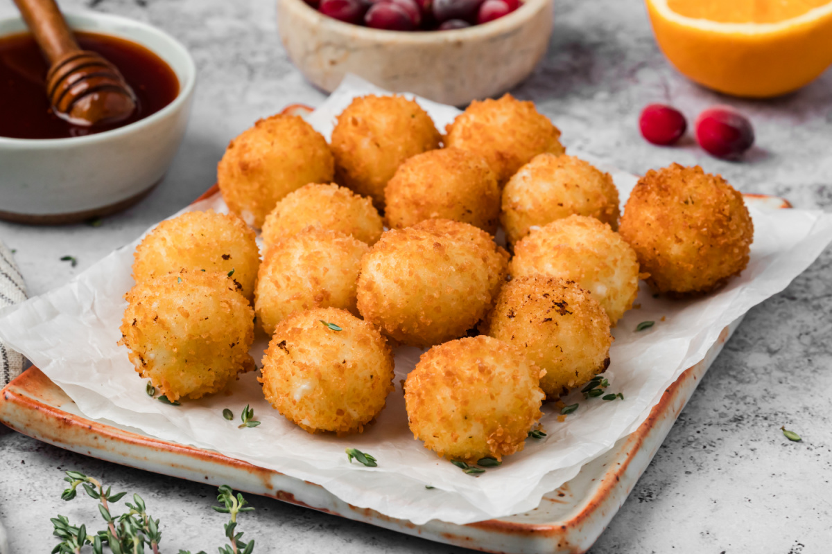 Crispy Fried Goat Cheese Balls with Panko Breadcrumbs Golden fried goat cheese balls coated in crispy panko breadcrumbs on a serving platter with cranberry hot honey on the side.