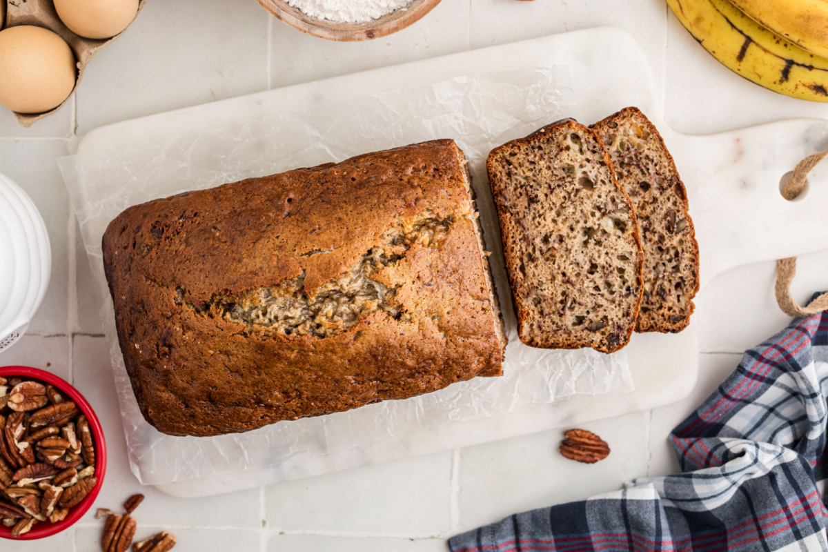Homemade banana bread loaf with two slices cut to show the banana and toasted pecans inside.