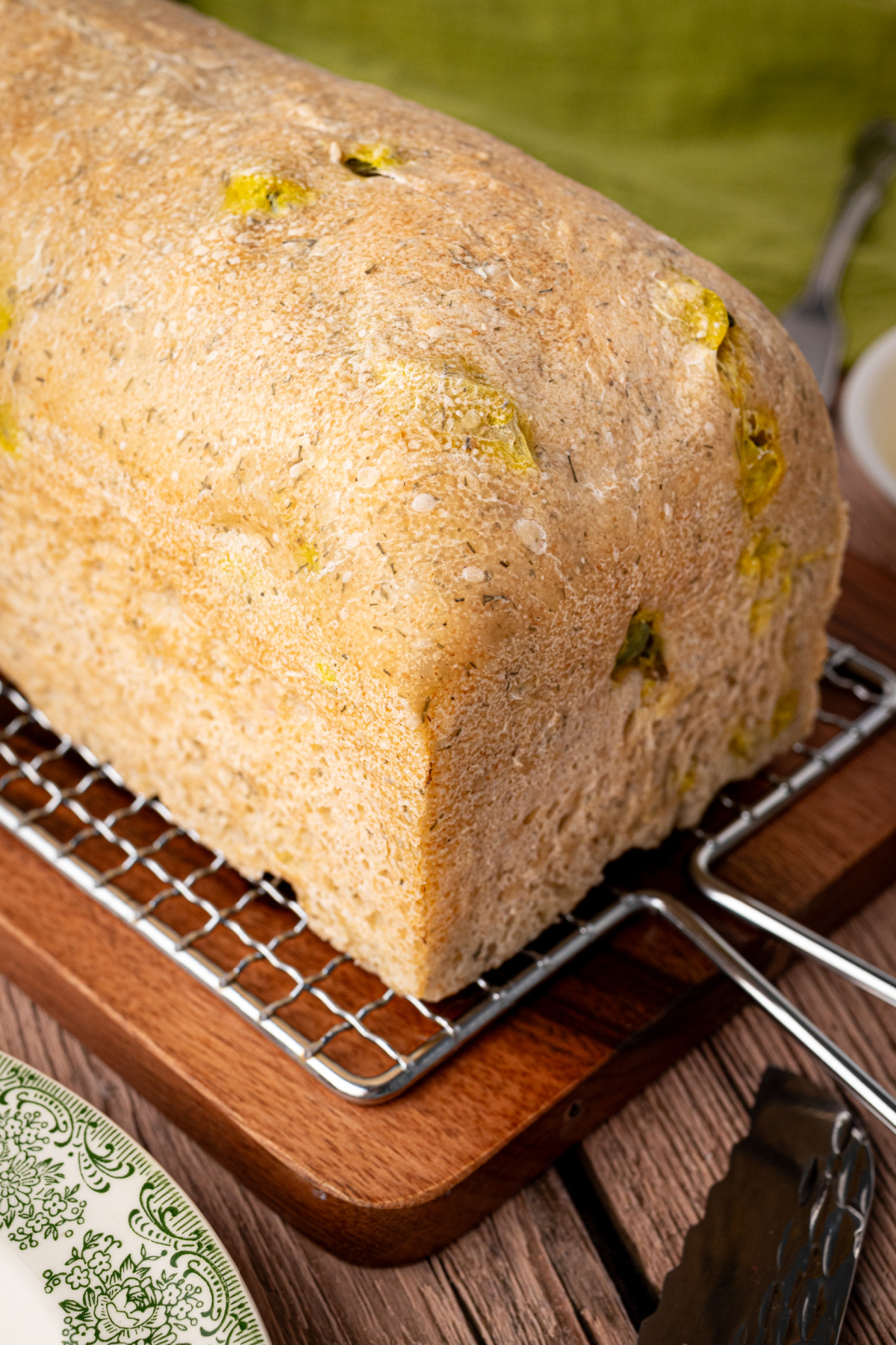 Whole loaf of homemade dill pickle sourdough bread cooling on a wire rack, with chopped pickles visible in the crust.