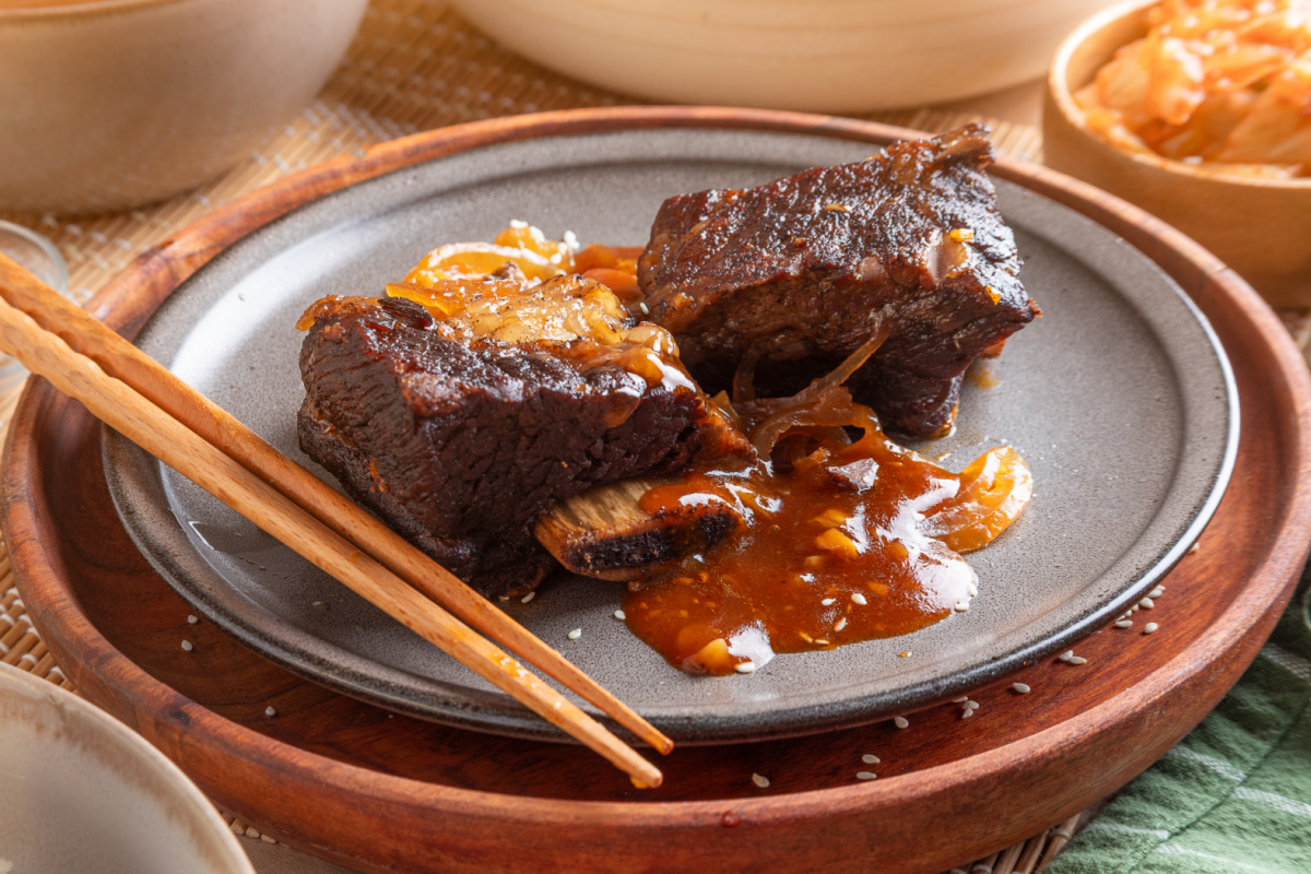Two Korean braised short ribs on a gray plate with softened onions and thickened gochujang sauce.