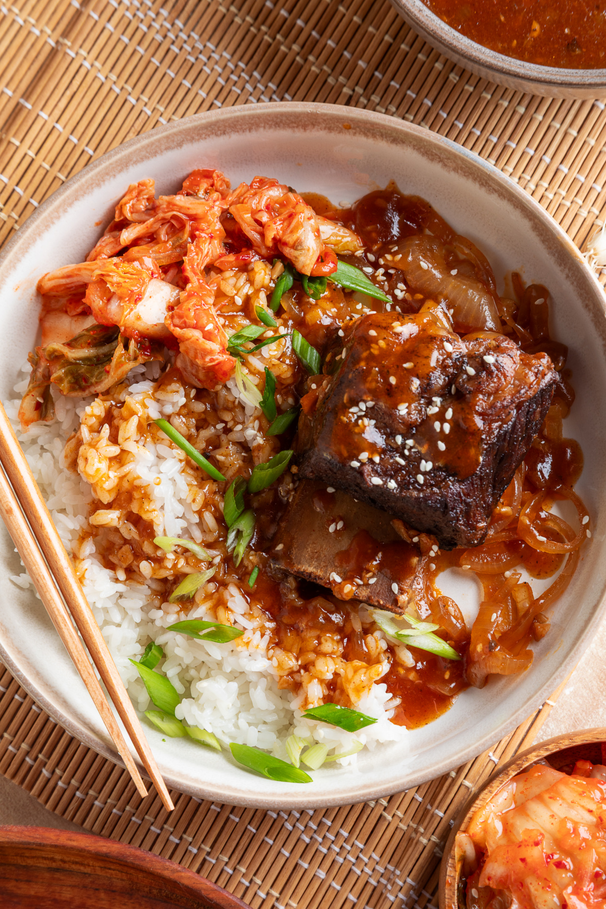 Korean braised short ribs served over white rice with gochujang sauce, kimchi, green onions, and sesame seeds.