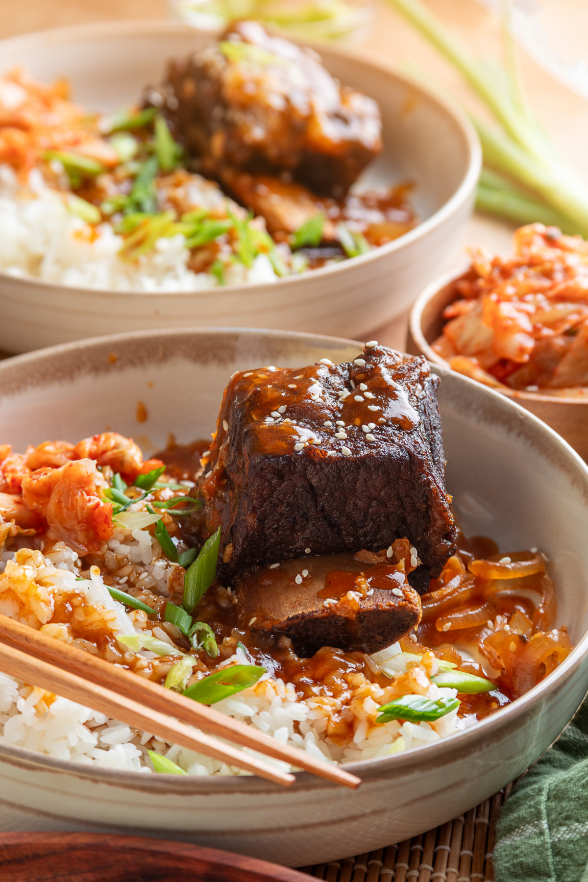 Korean braised short ribs over white rice with gochujang sauce, softened onions, green onions, sesame seeds, and kimchi.