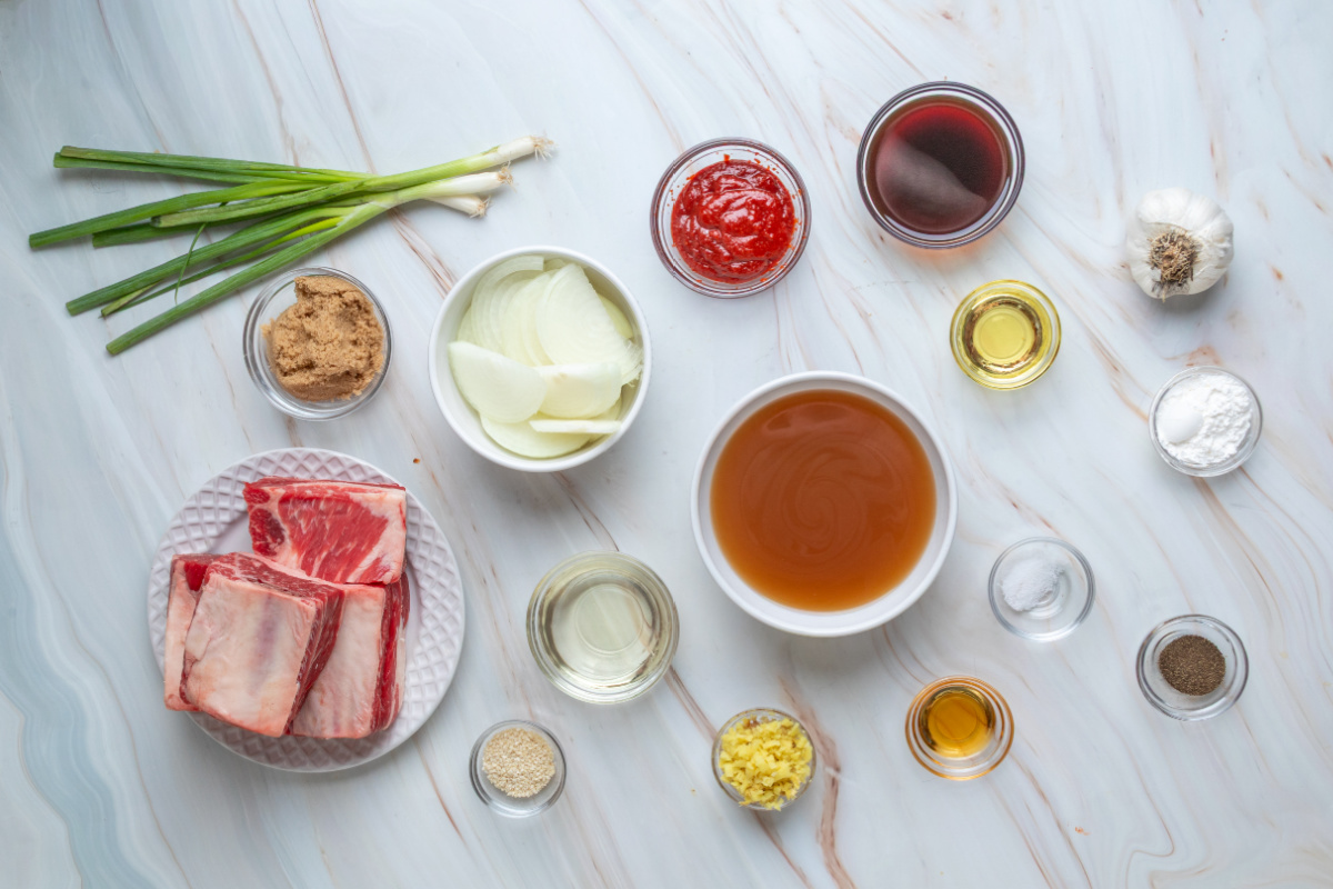 Ingredients for Korean braised short ribs, including bone-in beef, gochujang, brown sugar, ginger, garlic, soy sauce, beef stock, and onions.