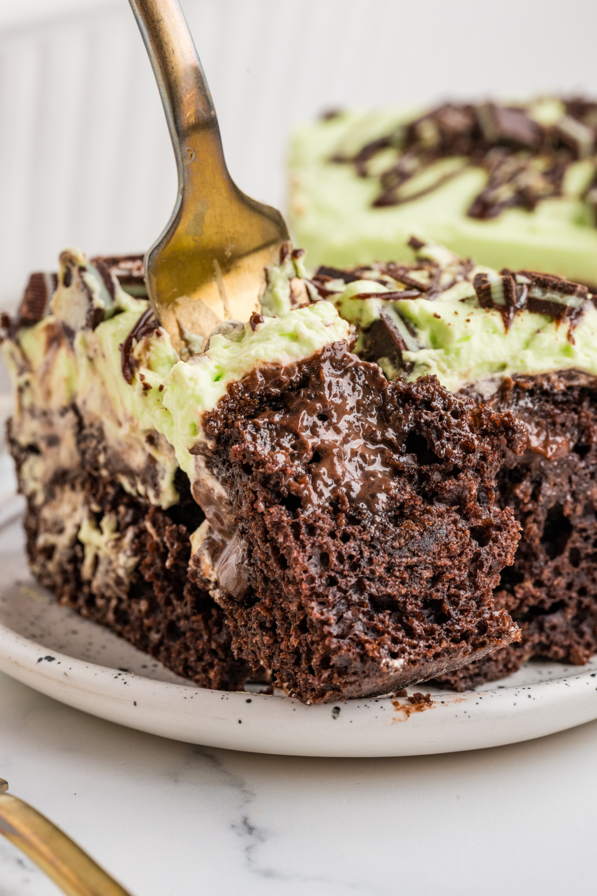 Mint chocolate poke cake with gooey hot fudge filling, pale green mint whipped cream and a fork lifting a bite.