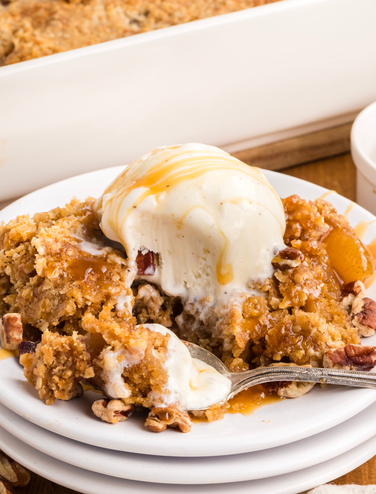 A spoonful of warm oatmeal cookie crust and cinnamon apples with melting vanilla ice cream, caramel drizzle, and chopped pecans. Spoonful of oatmeal cookie apple crisp with melting vanilla ice cream, caramel sauce, chopped pecans, and cinnamon apples.