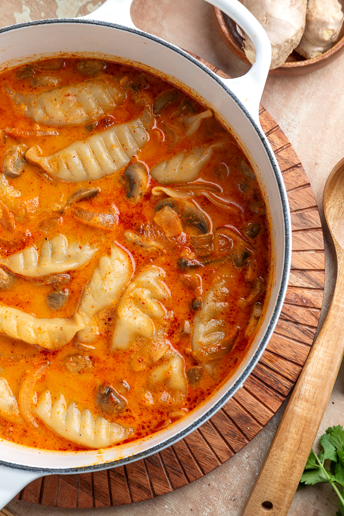 Coconut Red Curry Soup with Pork Potstickers Frozen pork potstickers and sliced mushrooms in a creamy orange coconut red curry broth inside a white Dutch oven.