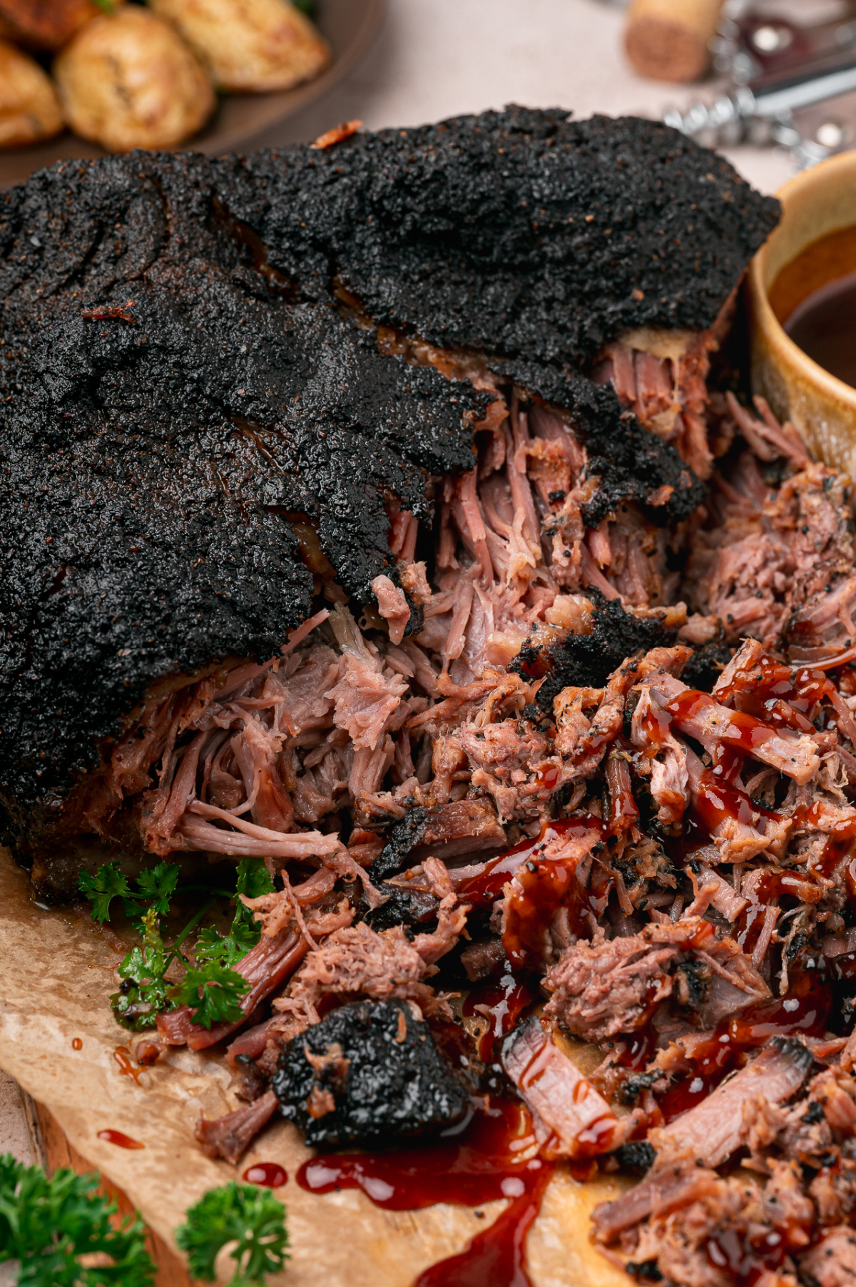 Tender pulled brisket beneath a nearly black coffee crust, with barbecue sauce drizzled over the shredded beef.