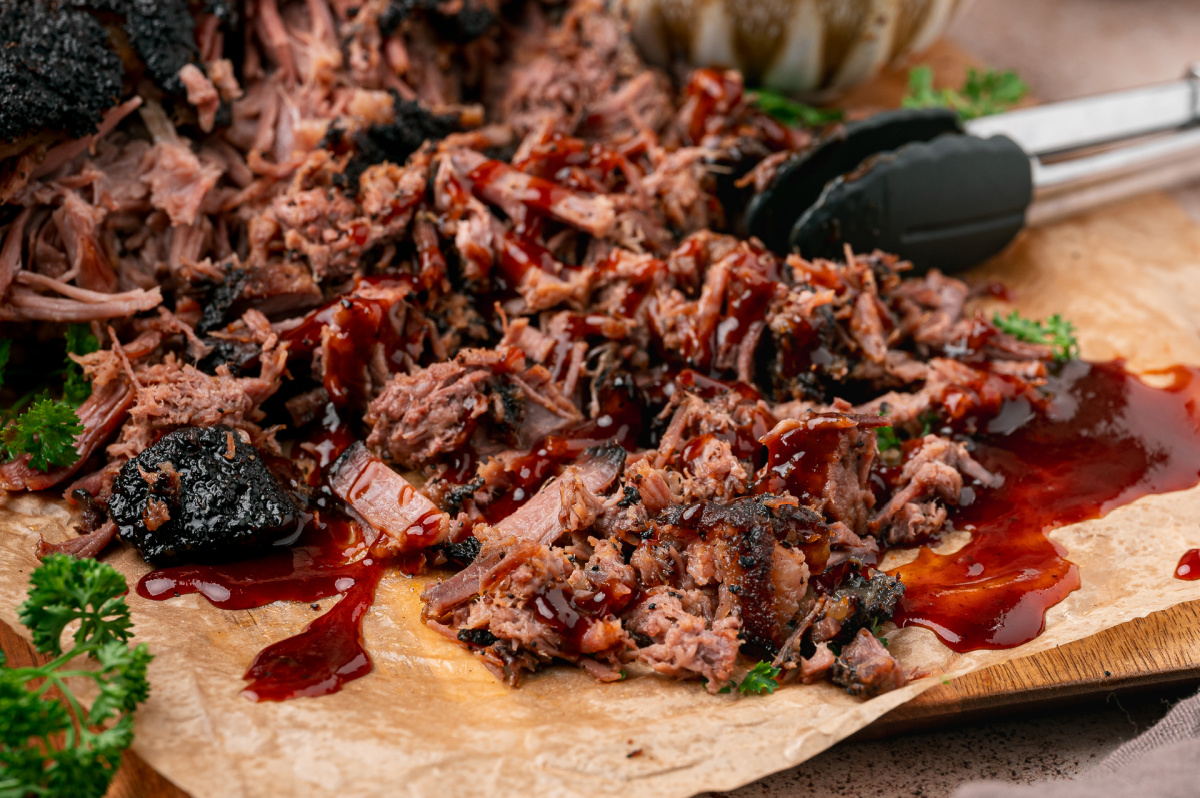 Tender pulled brisket with dark coffee crust and barbecue sauce spread across a wooden serving board.