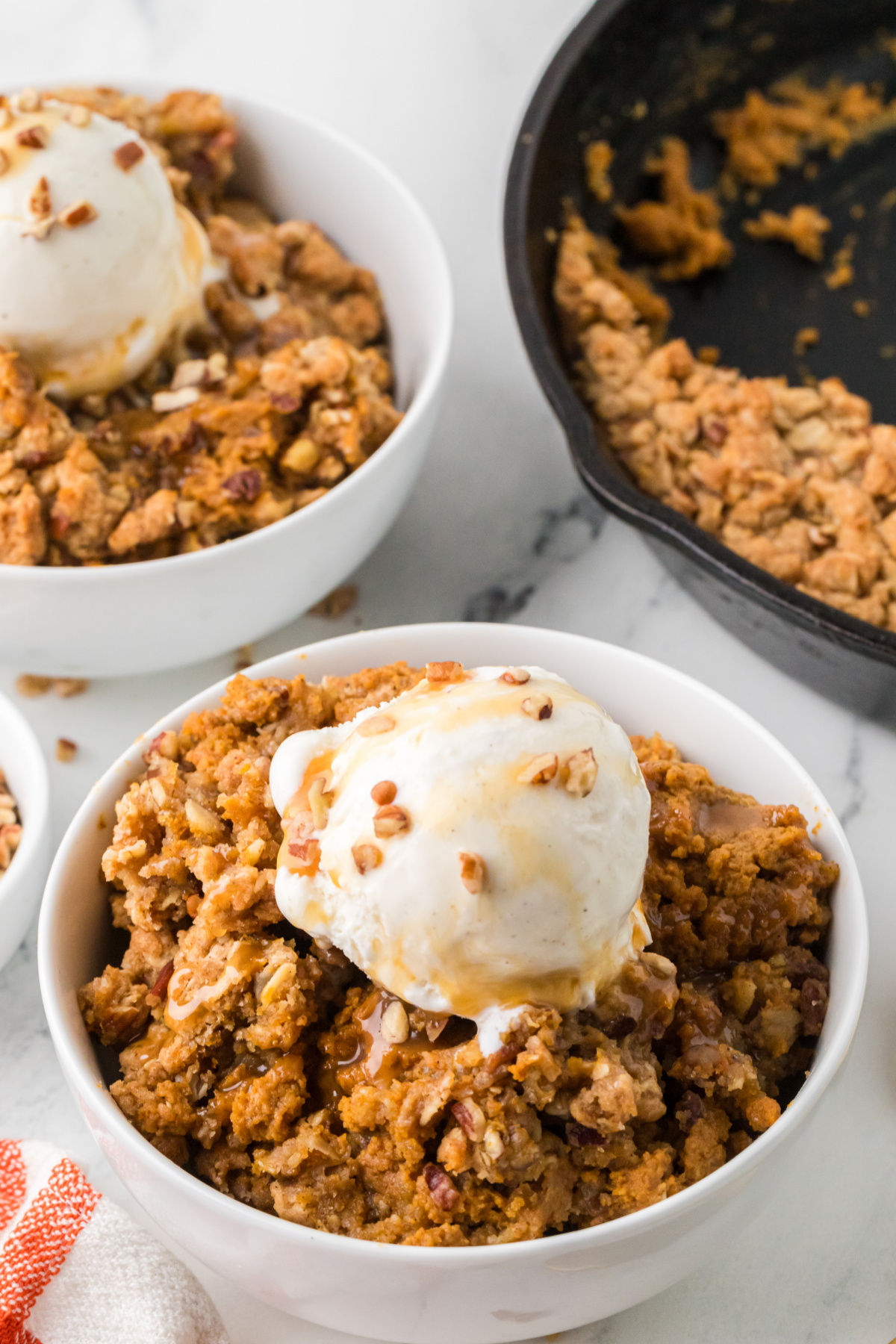 Warm pumpkin crisp with buttery oats, pecans, vanilla ice cream, and caramel drizzle. Pumpkin crisp with oat and pecan topping, vanilla ice cream, and caramel sauce served in a white bowl.
