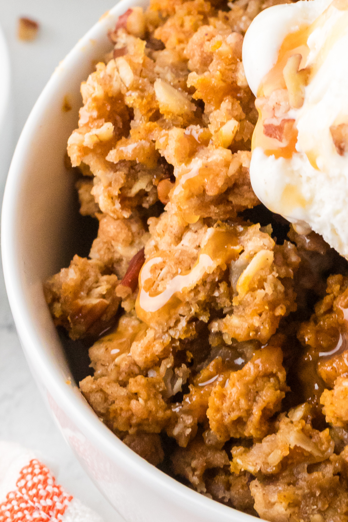 A close look at the soft spiced pumpkin filling, golden oat and pecan topping, and caramel melting into the warm dessert. Close-up of creamy pumpkin custard with buttery oat and pecan clusters, caramel sauce, and vanilla ice cream.