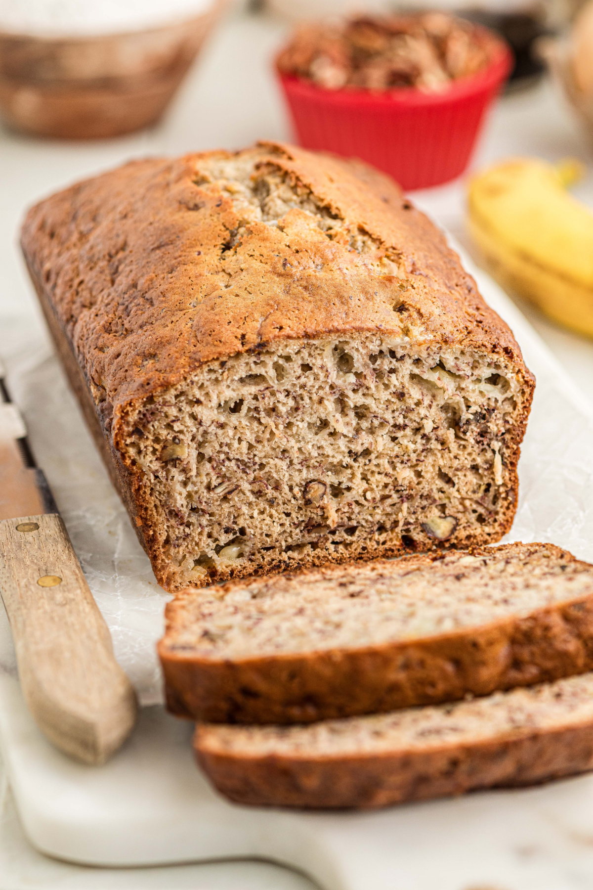 Sliced homemade banana bread showing toasted pecans and ripe banana throughout the loaf, with two slices in front.
