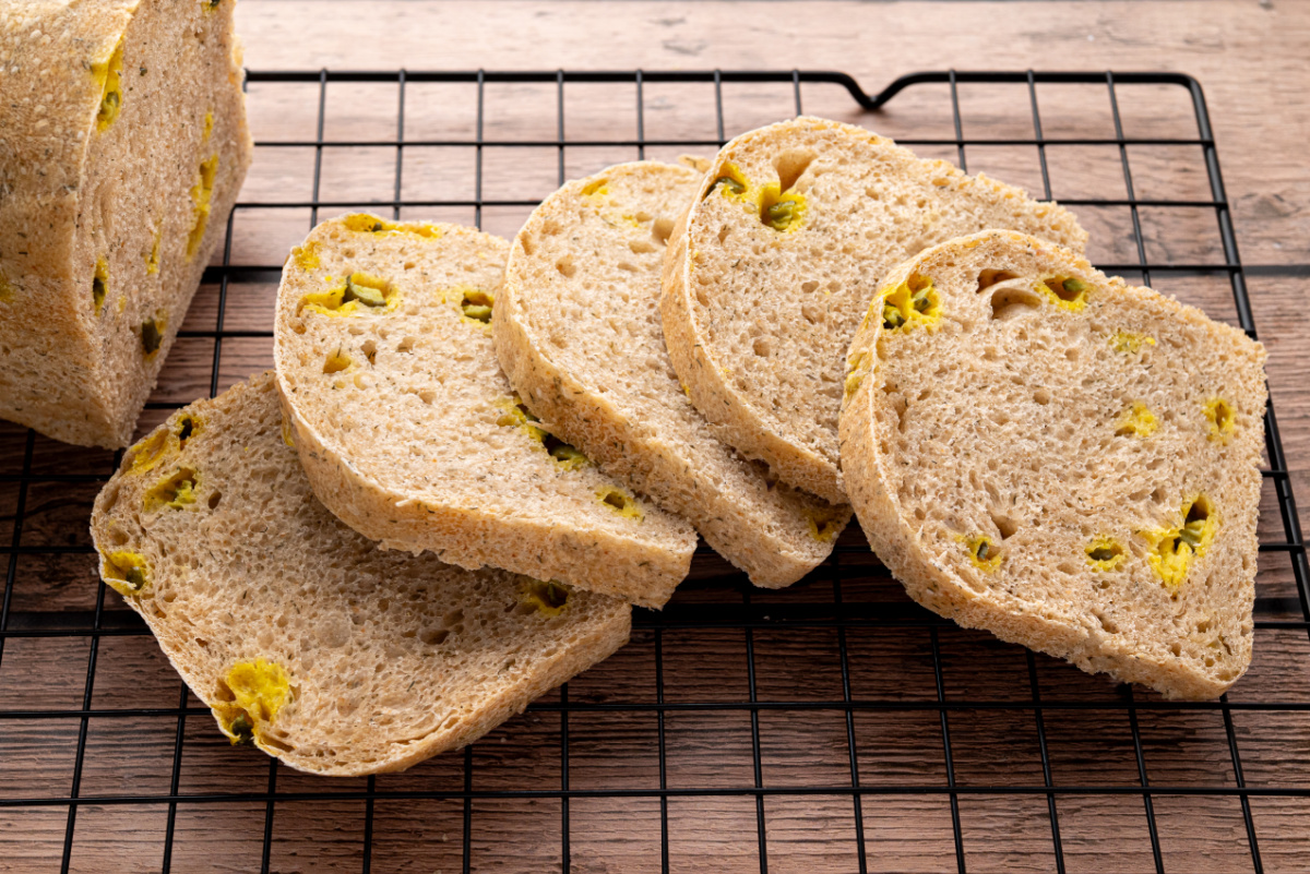 Slices of dill pickle sourdough sandwich bread arranged on a cooling rack, showing chopped pickles and the bread's interior texture.