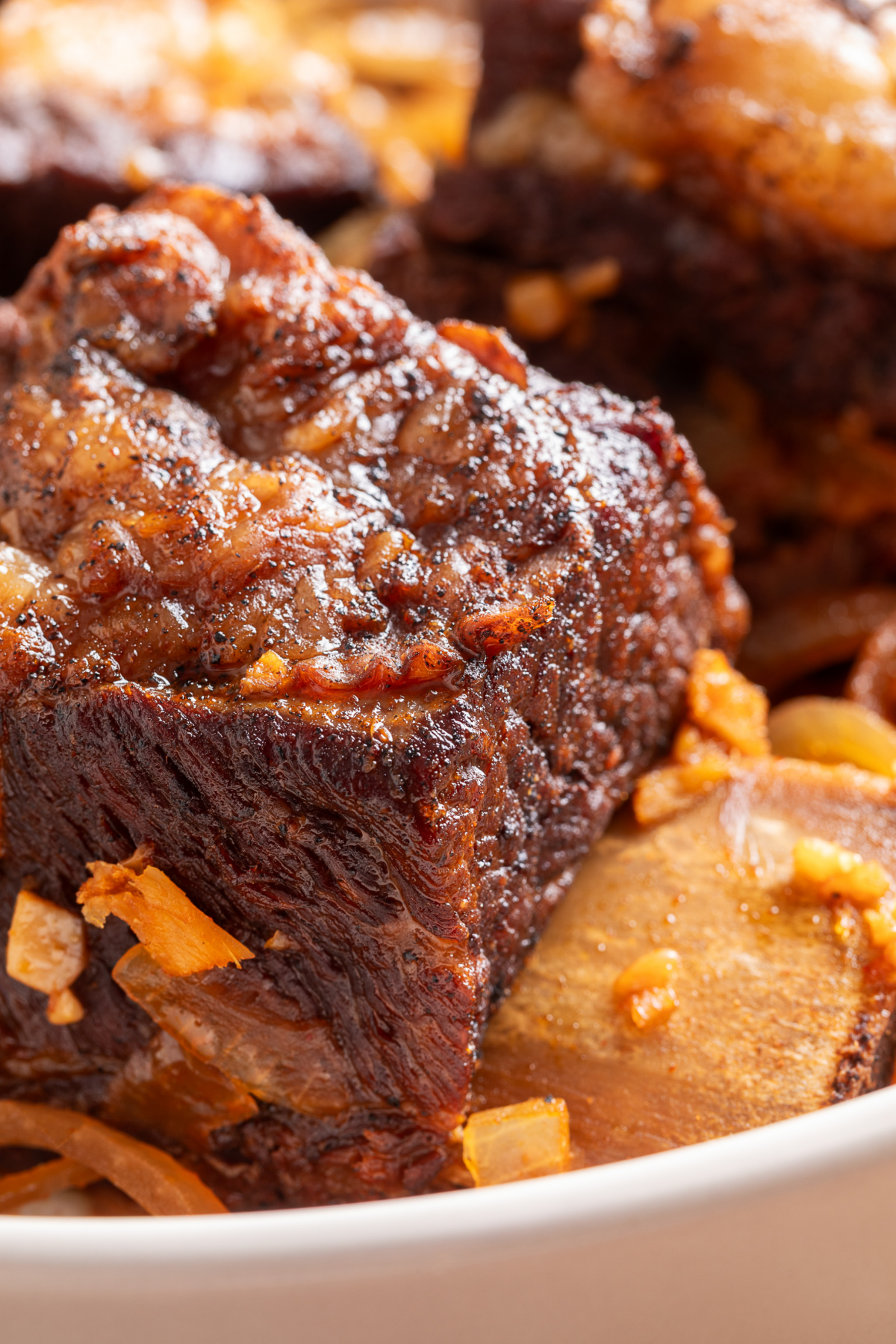 Close-up of tender bone-in beef short ribs with a dark brown exterior, softened onions, and sauce.
