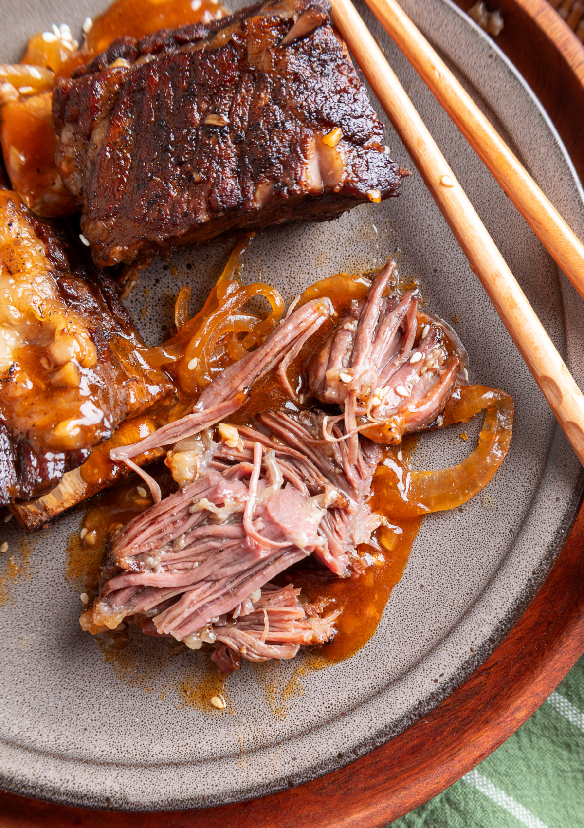 Fork-tender beef short ribs pulled apart on a gray plate with softened onions and gochujang sauce.