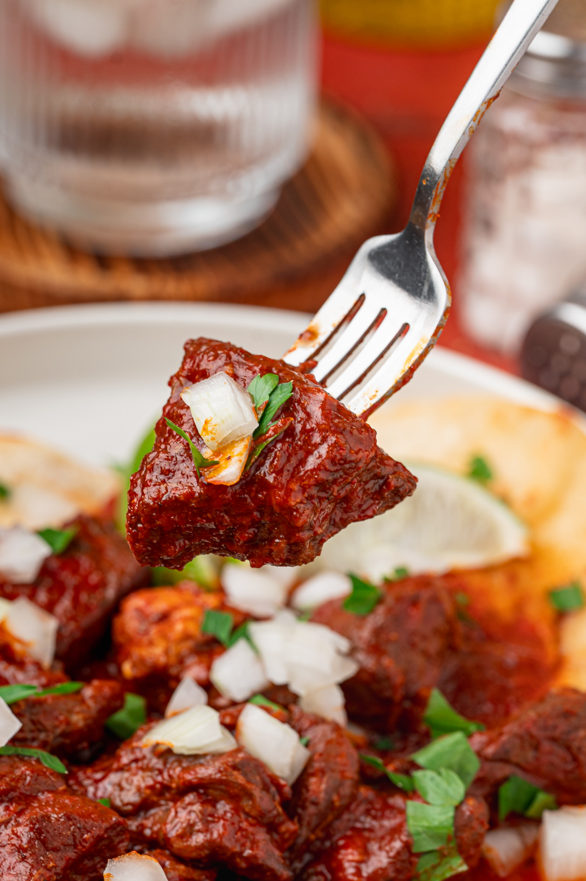 Fork holding a tender piece of pork shoulder coated in red chile sauce