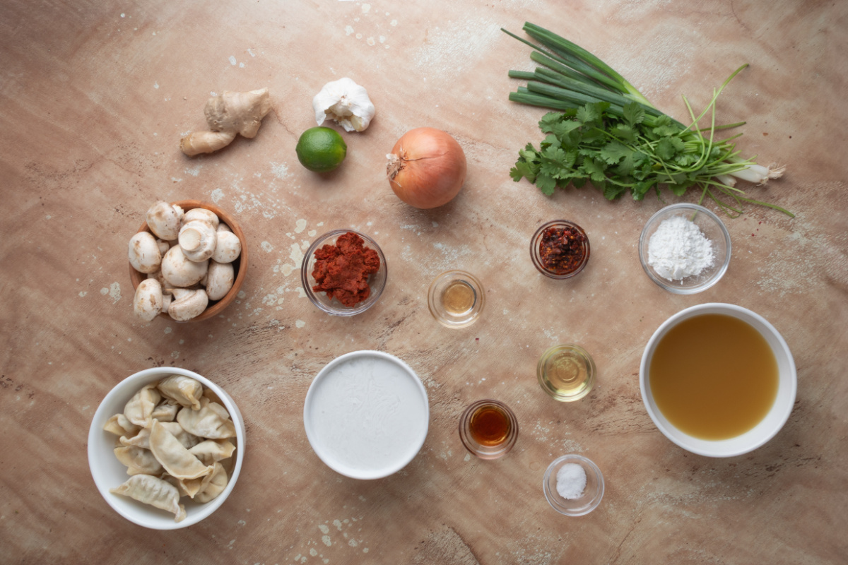 Ingredients for Thai Dumpling Soup with Coconut Red Curry Ingredients for Thai Dumpling Soup including frozen pork potstickers, red curry paste, mushrooms, ginger, garlic, lime, and fresh herbs.