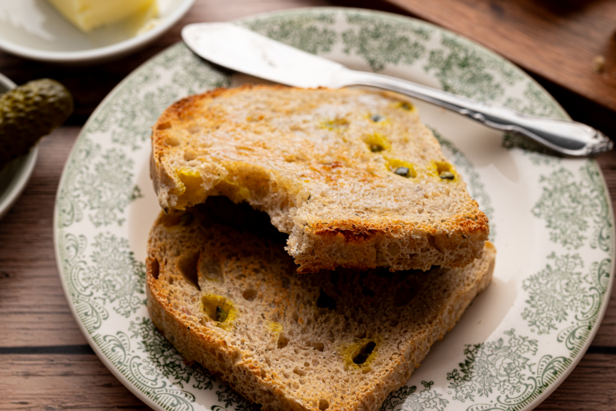 Two slices of toasted sourdough pickle bread with chopped dill pickles visible inside, served on a green patterned plate.